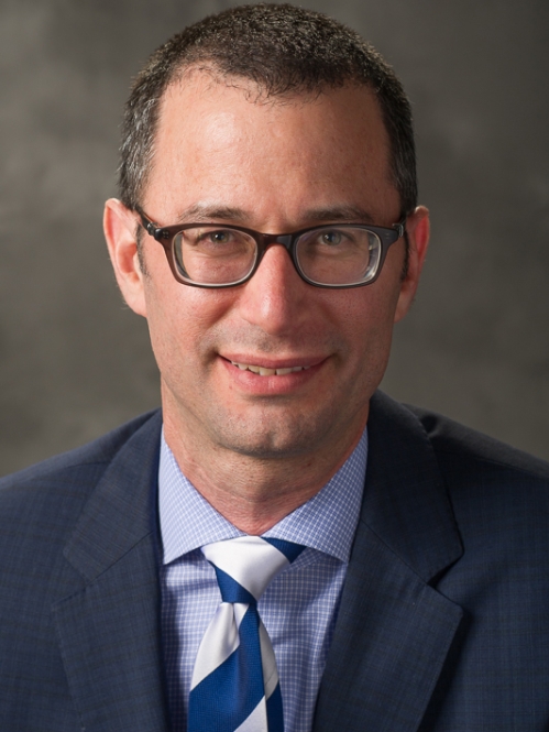 Man grinning who is wearing glasses and a blue tie
