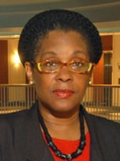 Woman grinning with glasses, wearing a red shirt and black suit jacket