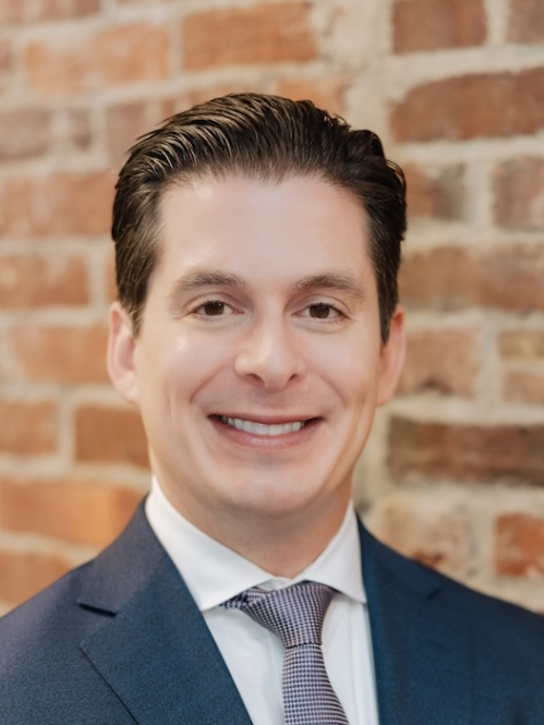 Man in blue suit smiling in front of brick wall