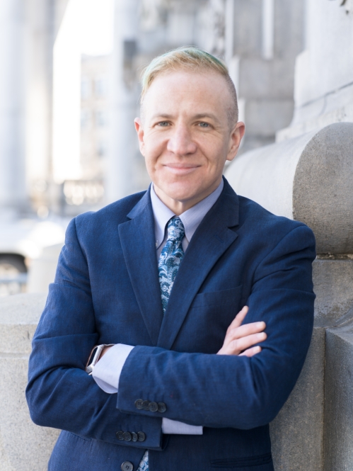 Man in blue suit smiling and leaning on building facade outdoors