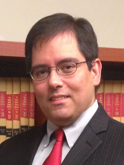 man in glasses and suit smiling in front of bookcase