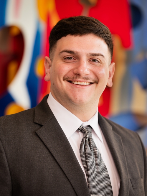 man smiling in suit and tie in front of colorful mural