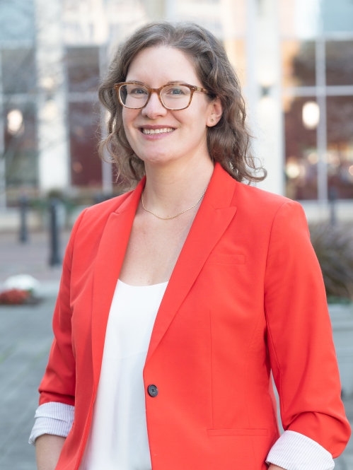 woman smiling outdoors in bright red/orange blazer and wearing glasses