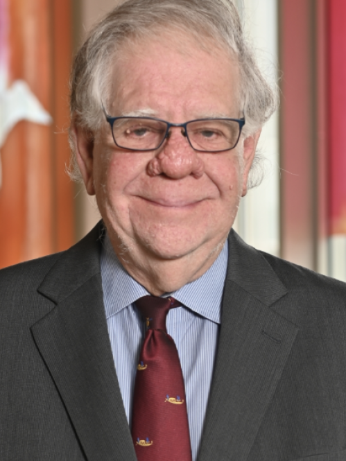 Man smiling, wearing glasses, a grey suit, a blue shirt, and a maroon tie. 