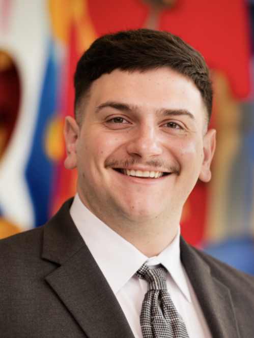 Man smiling wearing white buttoned shirt and dark colored suit jacket and tie. 