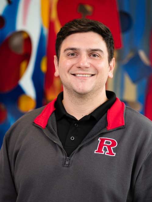man smiling in front of colorful art wearing 'R' shirt