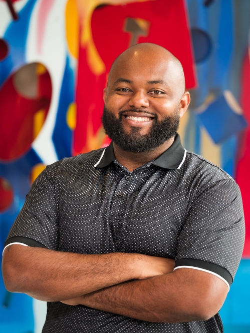man with beard and arms folded smiling in front of colorful art