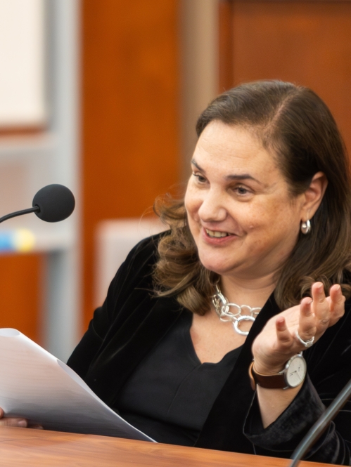 woman in black smiling and seated at table speaking into mic