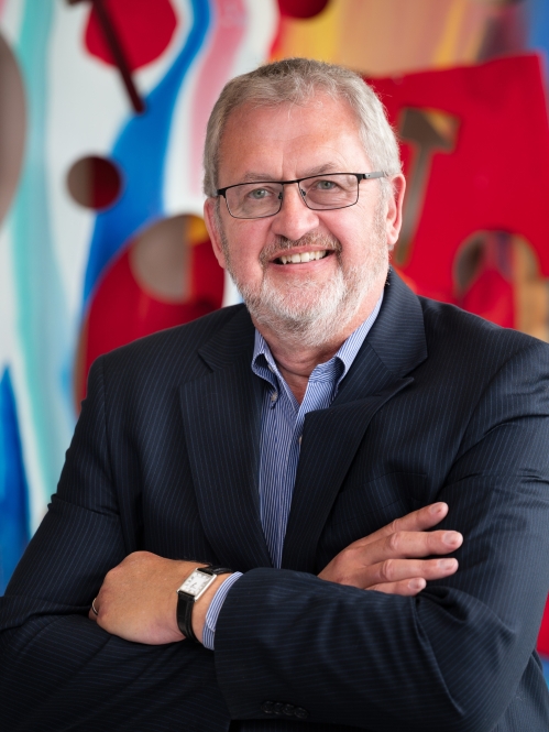 man wearing glasses smiling with arms crossed in front of colorful art