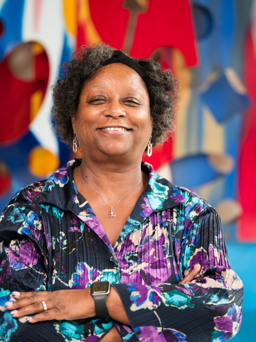 woman in colorful blouse smiling with arms folded in front of art