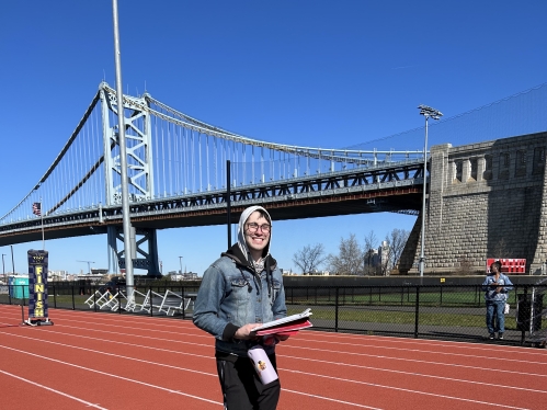 Student wearing hoodie on track with bridge in background