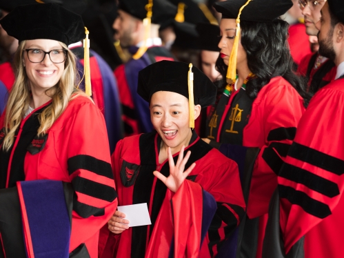 Graduate in cap and gown waving in commencement line