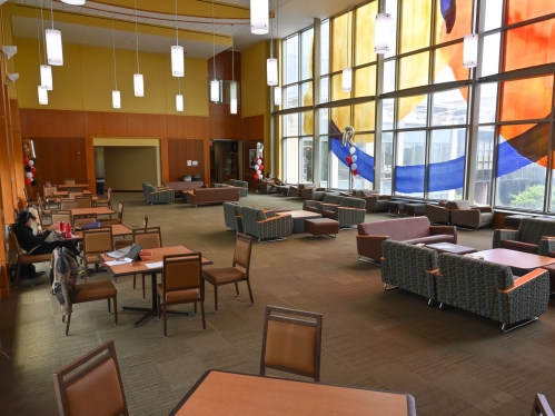 large hallway with tables, chairs and couches and large wall of windows