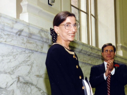 Photo of woman in black smiling and a man behind her applauding