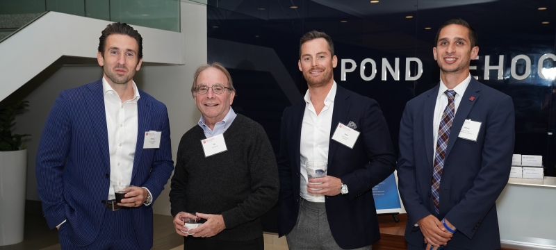 Four men standing and smiling holding drinks