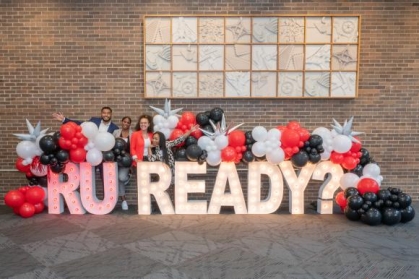 people posing for a photograph in front of balloons and a sign