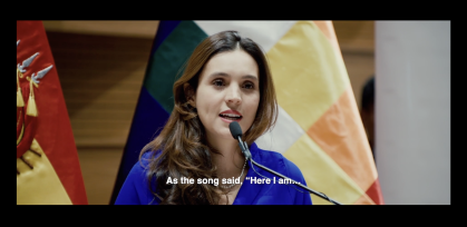 woman speaking at mic with flags behind her