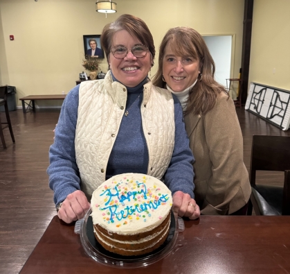 Two women posing behind 'happy retirement' cake