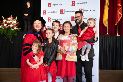 Woman in red robe and black cap posing for photos with husband and family