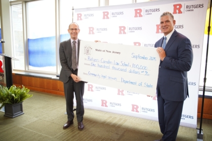 two men holding giant check in front of Rutgers Law step and repeat