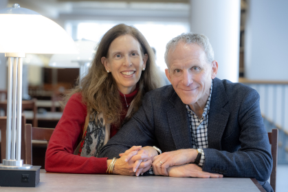 man and woman sitting next to each other with arms folded together at table in library