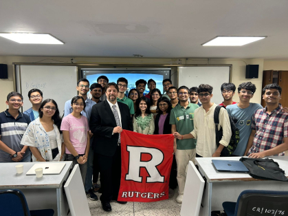 Picture of group of people in a classroom holding a Rutgers flag