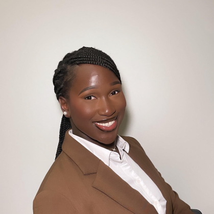 woman smiling and seated sideways in brown blazer and white blouse 