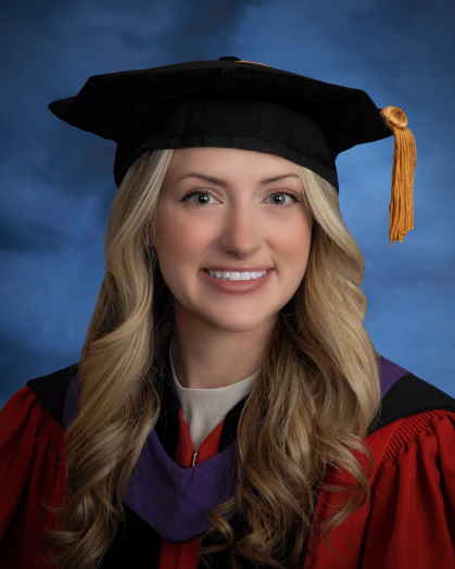 woman smiling wearing black commencement cap with purple hood and red and black robe