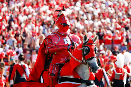 man in red knight uniform riding on horse with crowd behind him wearing red