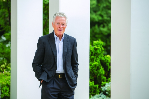 man standing by white columns with hand in pocket