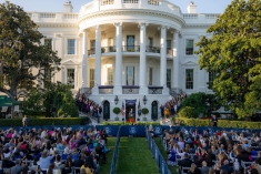 wide shot of the White House with people seated on the lawn