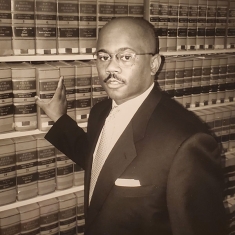 man in a suit posing for a photograph and standing in a library