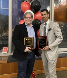 two men standing next to each other, holding awards, and posing for a photograph