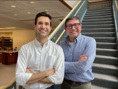 two men posing for a photograph in front of stairs