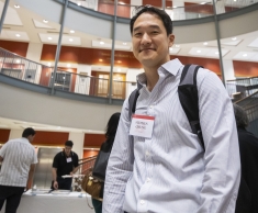man with black backpack and name tag smiling under spiral stairs
