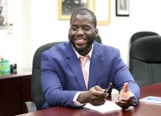 man in a suit sitting behind a desk and posing for a photograph