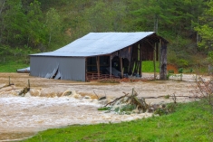 destroyed barn sitting amid brown flood waters