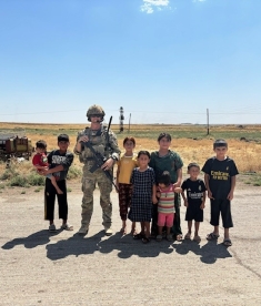man in army combat gear standing next to children
