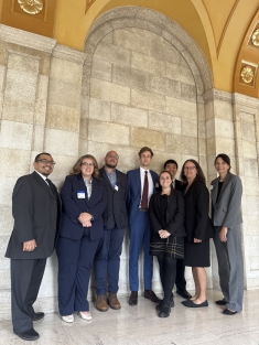 men and women in dark colored suits standing under arched columns inside building