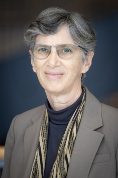 Woman grinning wearing glasses, turtleneck, suit jacket, and scarf 