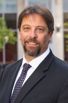 Man grinning wearing white button down shirt, blue tie, and suit jacket