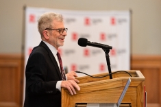 Man in suit and glasses smiling at a podium looking at audience