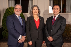 Two men and one woman smiling in dark suits