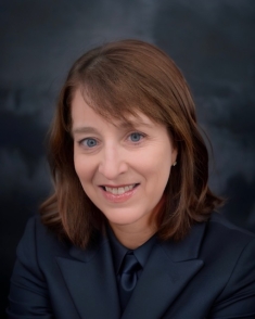 Woman in dark blue suit in front of dark blue photo backdrop