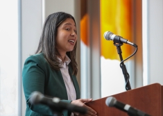 Woman in green blazer and white shirt speaking at podium