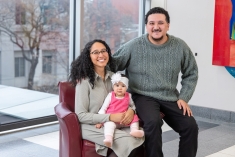 mom seated in armchair holding baby girl with dad seated on the arm