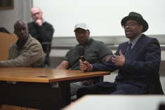 Group of three men seat at table with another at podium in the back