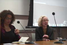 two women at table in front of classroom with mics