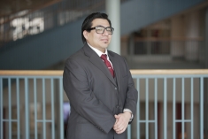 Man wearing glasses in grey suit and tie with hands together in front