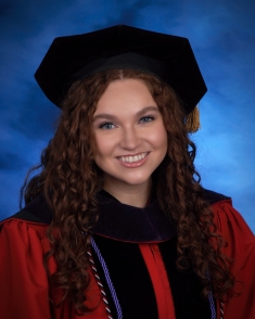 woman in black graduate cap and hood and red robe smiling against blue background
